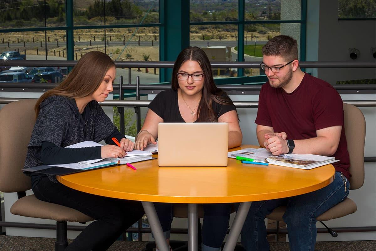 Three students at a table with one laptop